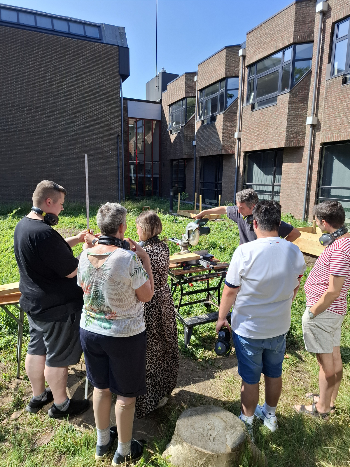 een workshopgever legt uit hoe de zaagmachine werkt aan enkele bezokers van Voluntas